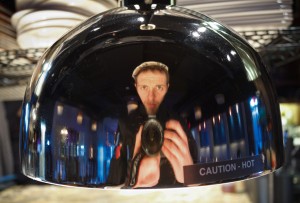 Bradley Miller takes a self-portrait in a metal food cover. Miller was named the head chef at Suzie’s Dogs and Drafts, a restaurant opening downtown. Photo courtesy of Bradley Miller.